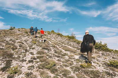 Rear view of hikers climbing mountain against sky