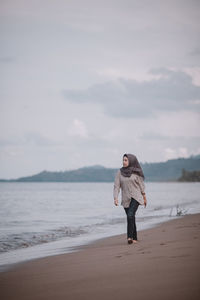 Full length of woman in hijab walking at beach against sky