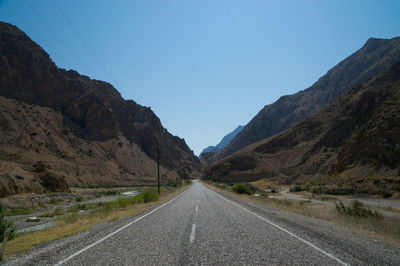 Empty road amidst mountains against clear blue sky