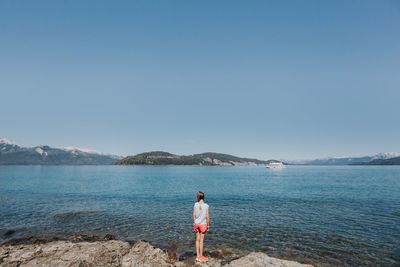 Rear view of young woman standing by sea against clear sky