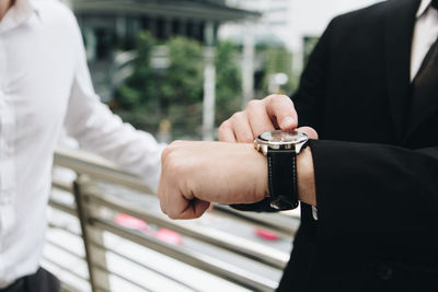 Midsection of businessman checking time by colleague standing on elevated walkway