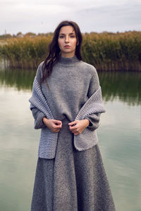 Woman stands next to the lake in a sweater and a scarf in the fall