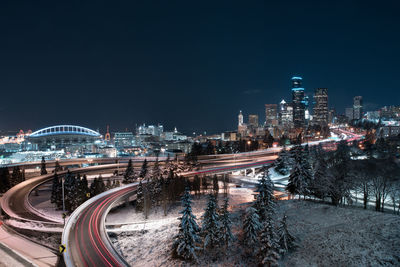 High angle view of light trails on road amidst buildings in city at night