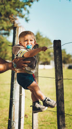 Cropped image of father holding boy by chainlink fence outdoors