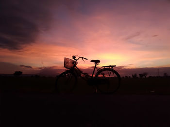 Silhouette bicycle on field against sky during sunset