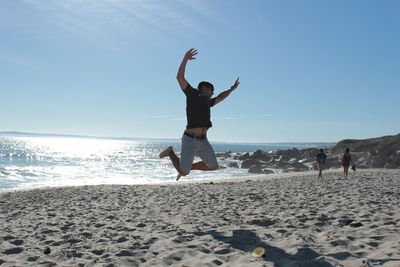 Full length of man jumping on beach against clear sky