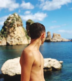 Midsection of shirtless man on rock against sea