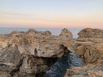 Rocks on shore against sky during sunset