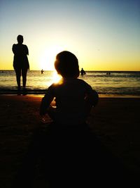 Silhouette of people standing on beach at sunset