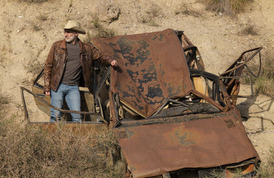 Adult man in cowboy hat with abandoned car in desert, almeria, spain