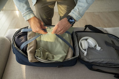Young man packing clothes in backpack on sofa