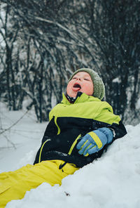 Boy sitting in snow on field during winter