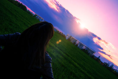 Rear view of woman on grassy field against sky during sunset