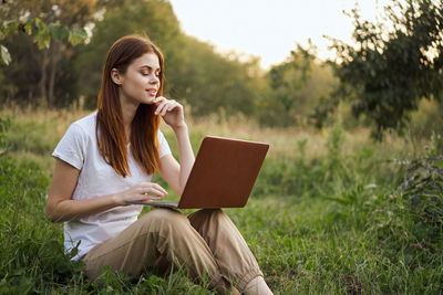 Young woman using laptop while sitting on field