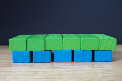 Close-up of green and blue blocks arranged on wooden table against black background