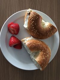 Directly above shot of bagel with cream cheese and sliced strawberries in plate on wooden table