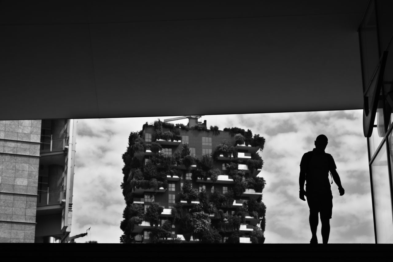 REAR VIEW OF SILHOUETTE MAN STANDING BY CITY AGAINST SKY