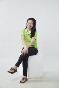 Portrait of smiling young woman sitting against white background