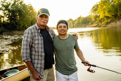 Portrait of friends standing at lakeshore against clear sky during sunset