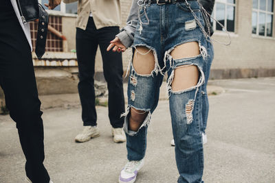 Low section of woman wearing torn jeans dancing with friends on street