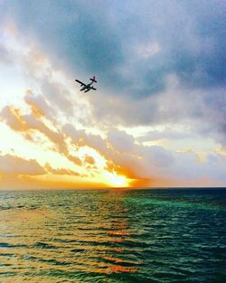 Airplane flying over sea against sky during sunset