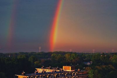 Rainbow over building against sky at sunset