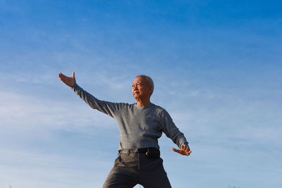 Low angle view of senior man exercising against blue sky