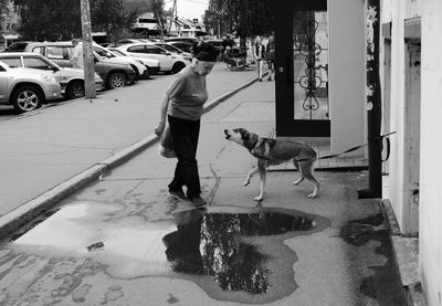 Side view of senior woman standing by dog barking on footpath