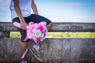 Midsection of woman with pink flower against wall