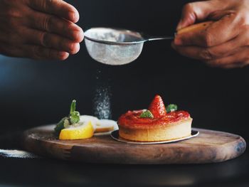 Cropped image of hand sprinkling sugar on strawberry tart