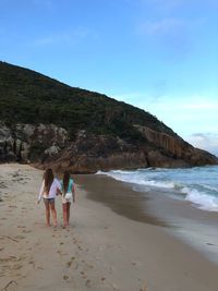 Rear view of girls walking at beach against sky