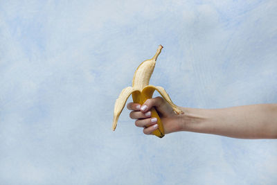 Close-up of woman holding banana against sky