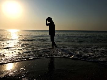 Silhouette man standing on beach against sky during sunset