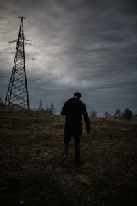 Rear view of man walking on field against cloudy sky at dusk