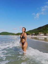 Portrait of young woman standing in sea against sky