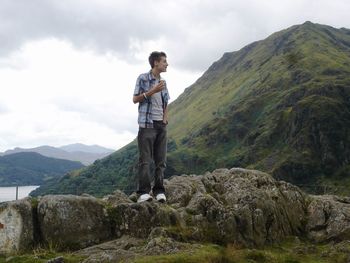 Full length of young man eating ice cream cone while standing on rock against sky