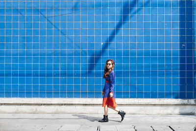 Portrait of smiling young woman walking by wall outdoors