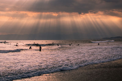 People at beach against sky during sunset