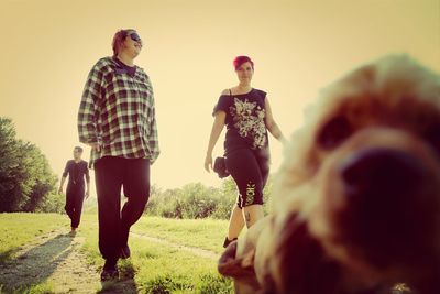 Rear view of friends standing on field against clear sky