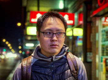 Portrait of young man on city pavement against neon signs at night.