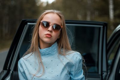 Portrait of young woman wearing sunglasses by car