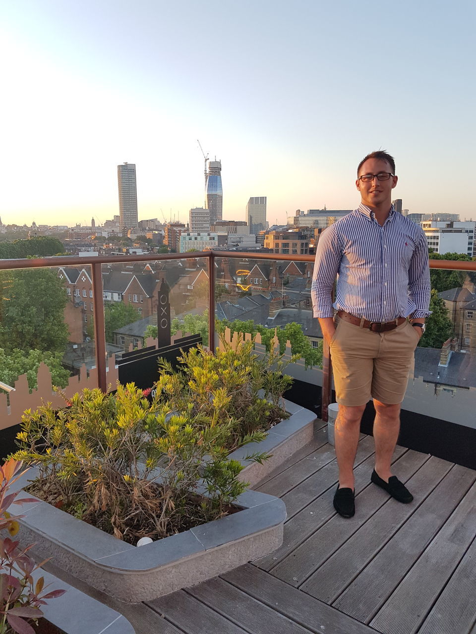 architecture, casual clothing, portrait, real people, built structure, lifestyles, looking at camera, full length, one person, bridge - man made structure, leisure activity, smiling, standing, outdoors, city, building exterior, happiness, cityscape, young adult, day, sky, people