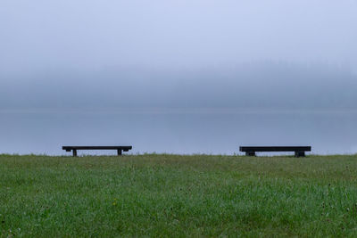 Empty bench on field against sky