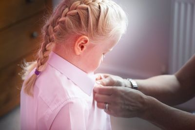 Cropped hands of mother closing daughter shirt button at home