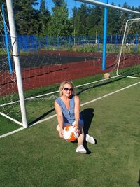 Full length of young woman sitting on soccer field