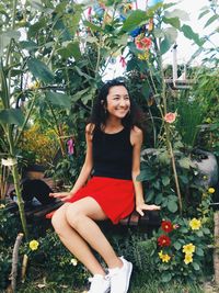 Portrait of smiling young woman sitting on grass against trees
