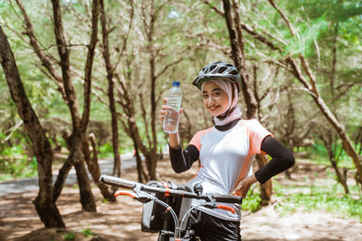 Smiling woman holding water bottle against tree