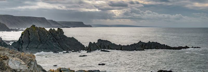 Scenic view of sea and rocks against cloudy sky