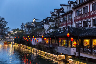 Canal by illuminated buildings against sky at dusk