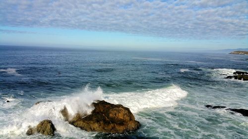 Scenic view of sea and waves crashing against rocks and sky